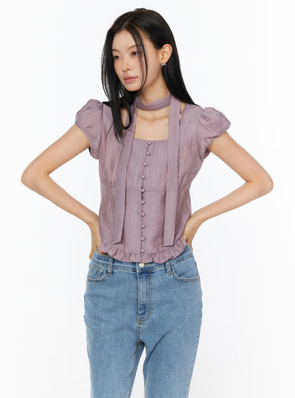 Puff Sleeve Shirred Blouse with Scarf IU519 in purple, 3/4 front view on model with hands on hips, puff sleeves, square neck, button-front placket, ruffled hem, and scarf, with blue jeans.
