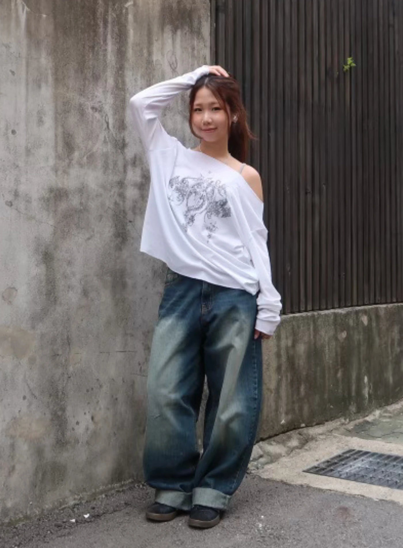 Leilani Washed Baggy Jeans CM531 in dark blue, outdoor street full-body shot on model, wide-fit washed denim styled with oversized white graphic long-sleeve top and sneakers.