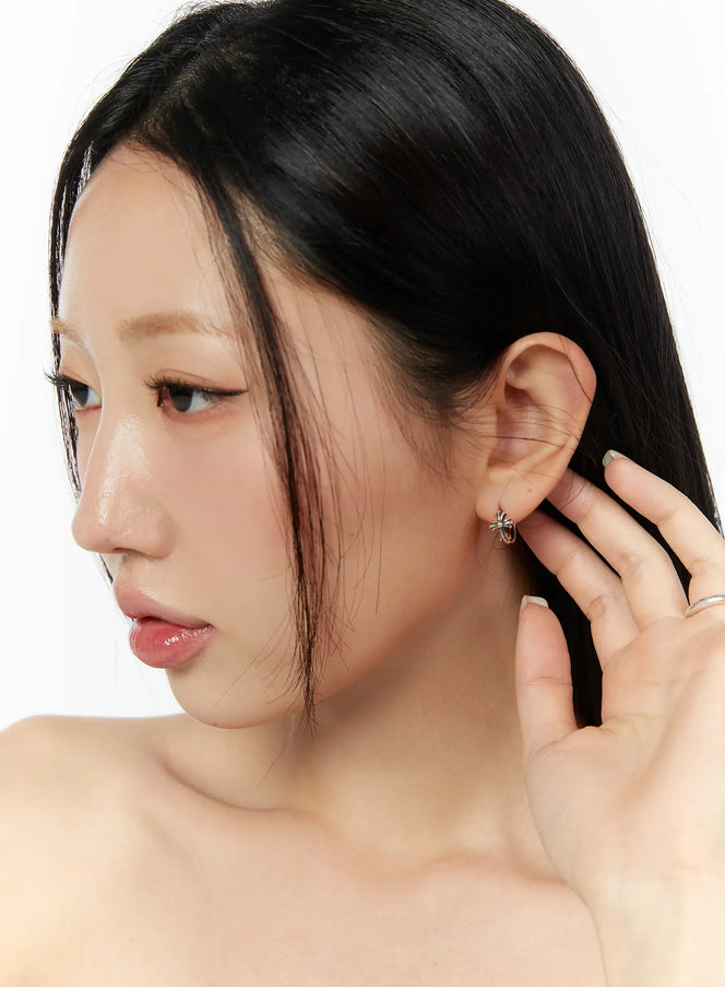 Theo Earring IU503 in silver, side close-up worn on model, cross charm huggie hoop at ear, minimal classic acubi styling.