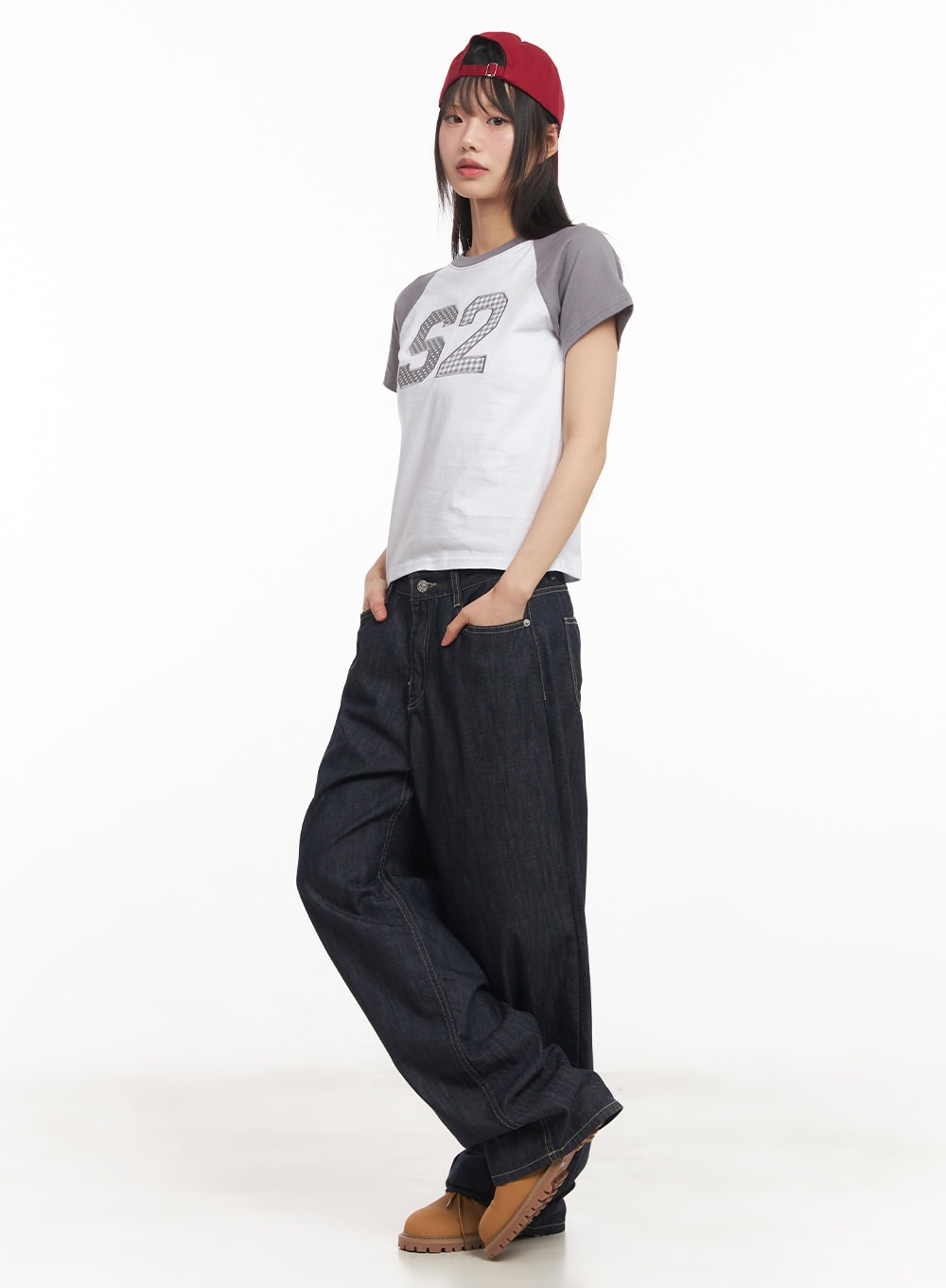 Ivara Wide-Leg Jeans CA522 in dark blue, diagonal side view on model, relaxed low-rise wide-leg denim with contrast topstitching, hand in pocket, styled with cropped raglan tee and red cap.