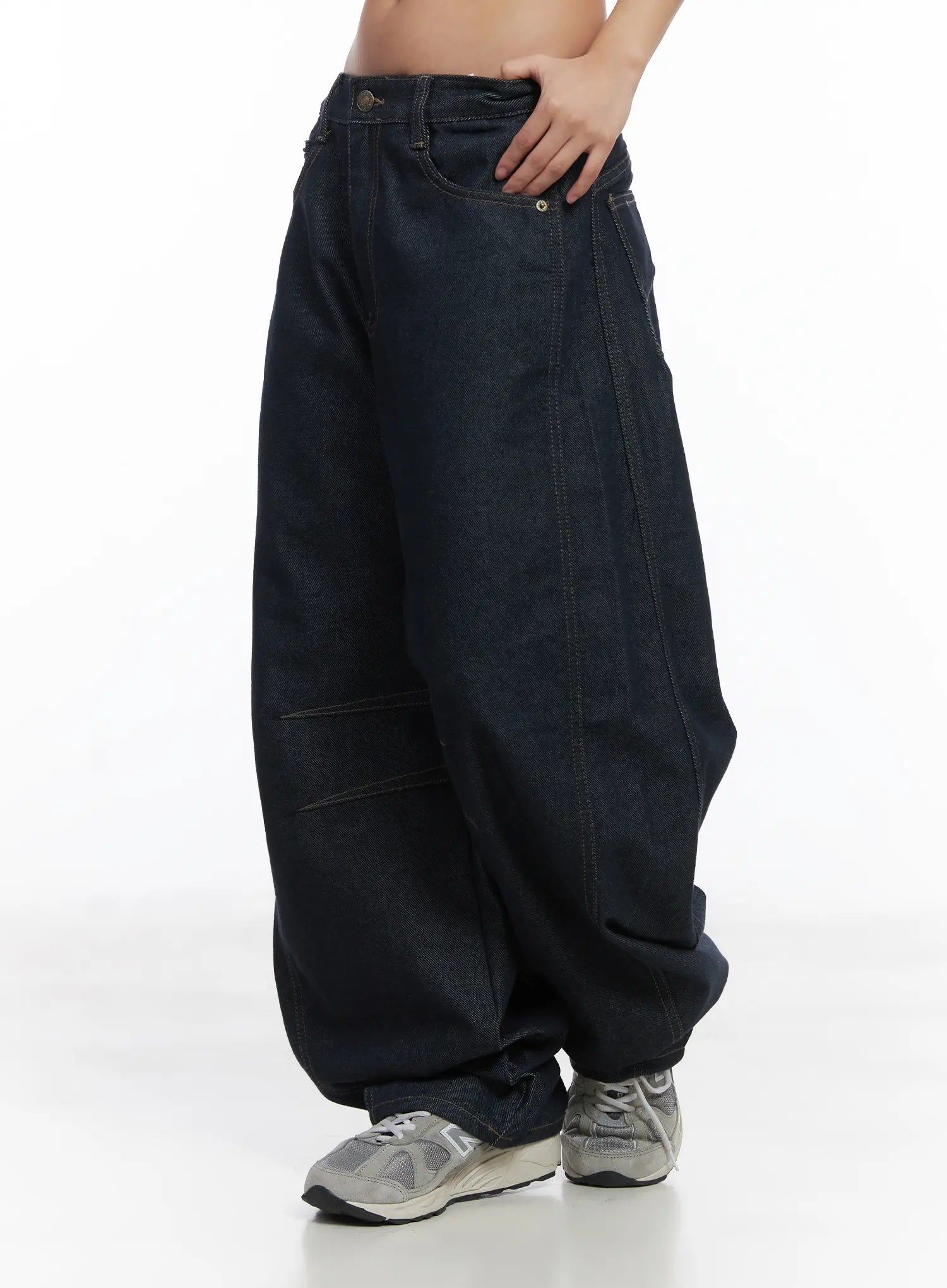Mingyu Wide Jeans CJ512 in dark blue, side full-length view on model, emphasizing the exaggerated balloon wide-leg volume, knee panel seam, and long hem over grey sneakers.