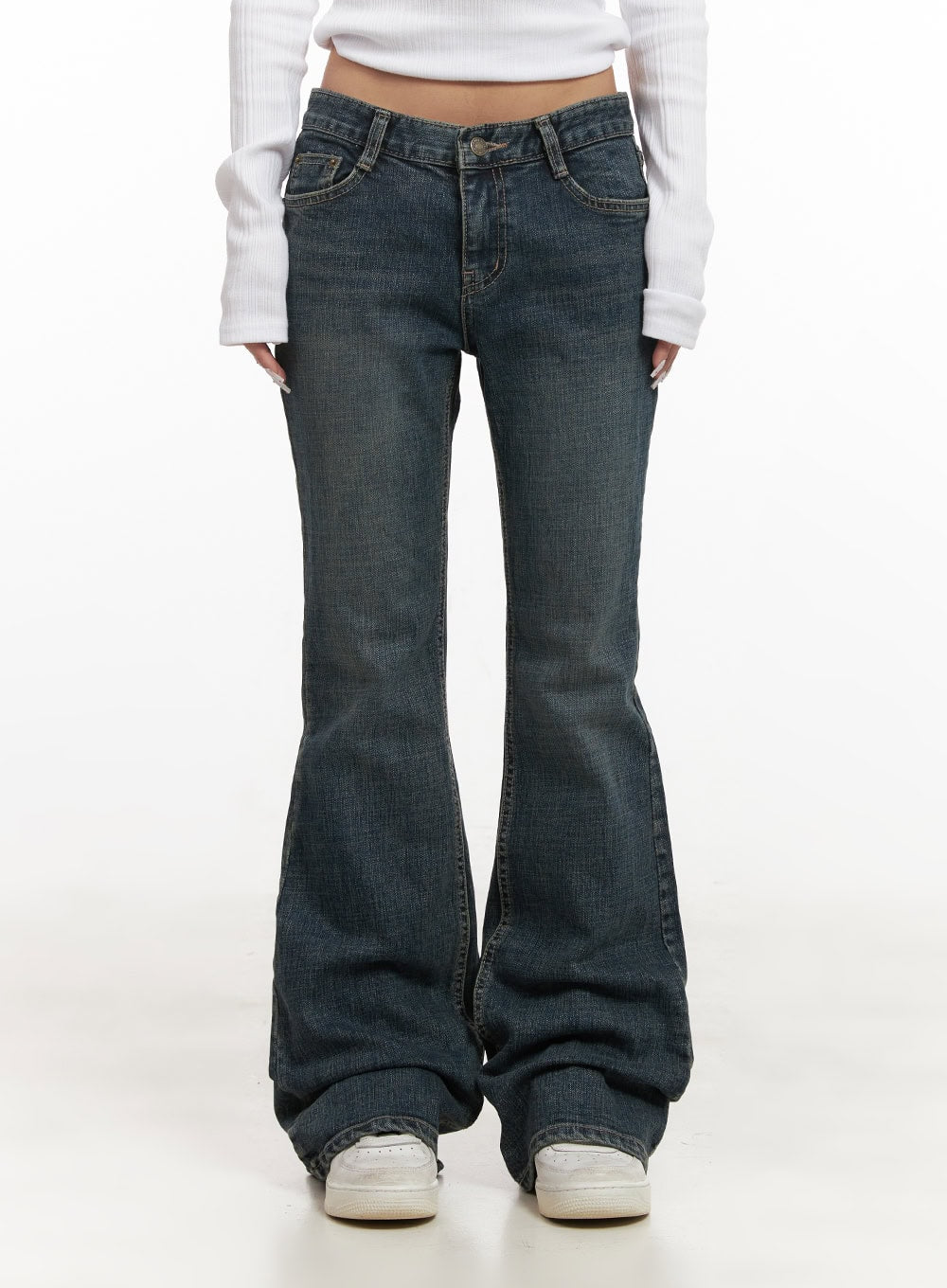 Natalia Low-Rise Flared Jeans CJ508 in dark blue, front waist-to-hem close-up on model, low-rise five-pocket washed denim, pronounced bootcut flare pooling over white sneakers, ribbed white top tucked slightly.