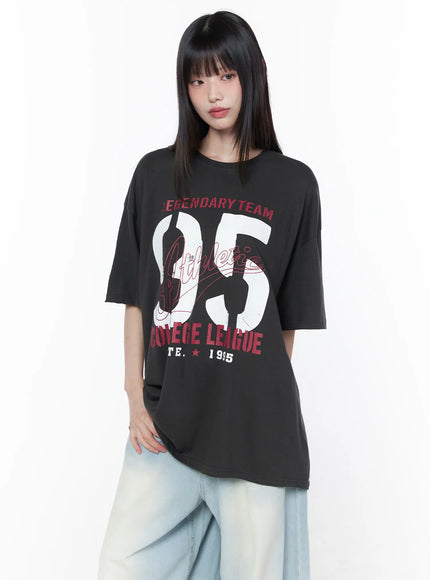 Oversized Graphic Tee CU519 in dark gray, front upper-body shot on model, showcasing crew neckline, short drop-shoulder sleeves, and full collegiate 95 graphic, paired with wide-leg jeans.