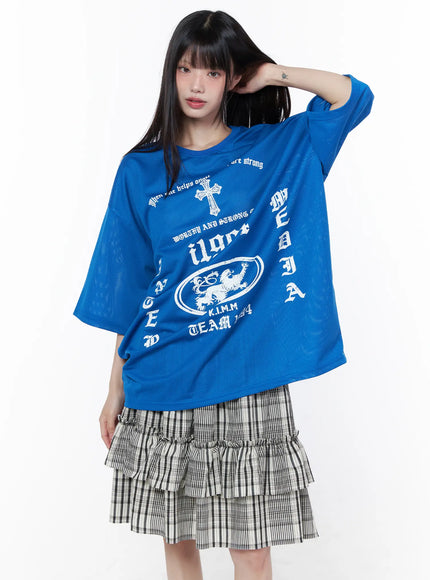 Oversized Mesh Graphic Tee CU519 in Blue M/L, front angled shot on model with hand raised, semi-sheer mesh fabric, white gothic graphic prints, oversized fit, styled with plaid ruffle mini skirt.