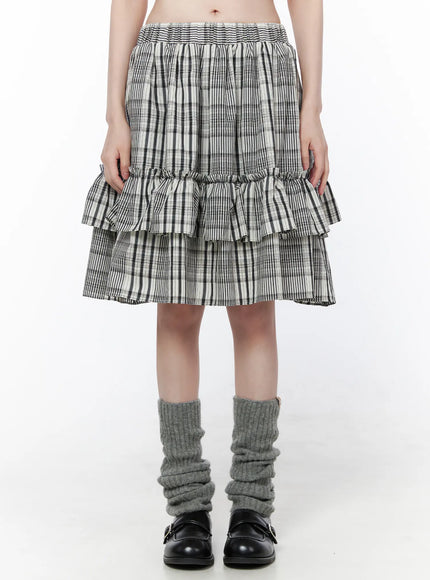 Plaid Layered Midi Skirt CU519 in black, front mid-shot on model standing, full skirt length visible with two ruffle tiers, elastic waist, black-white plaid, grey leg warmers and loafers.