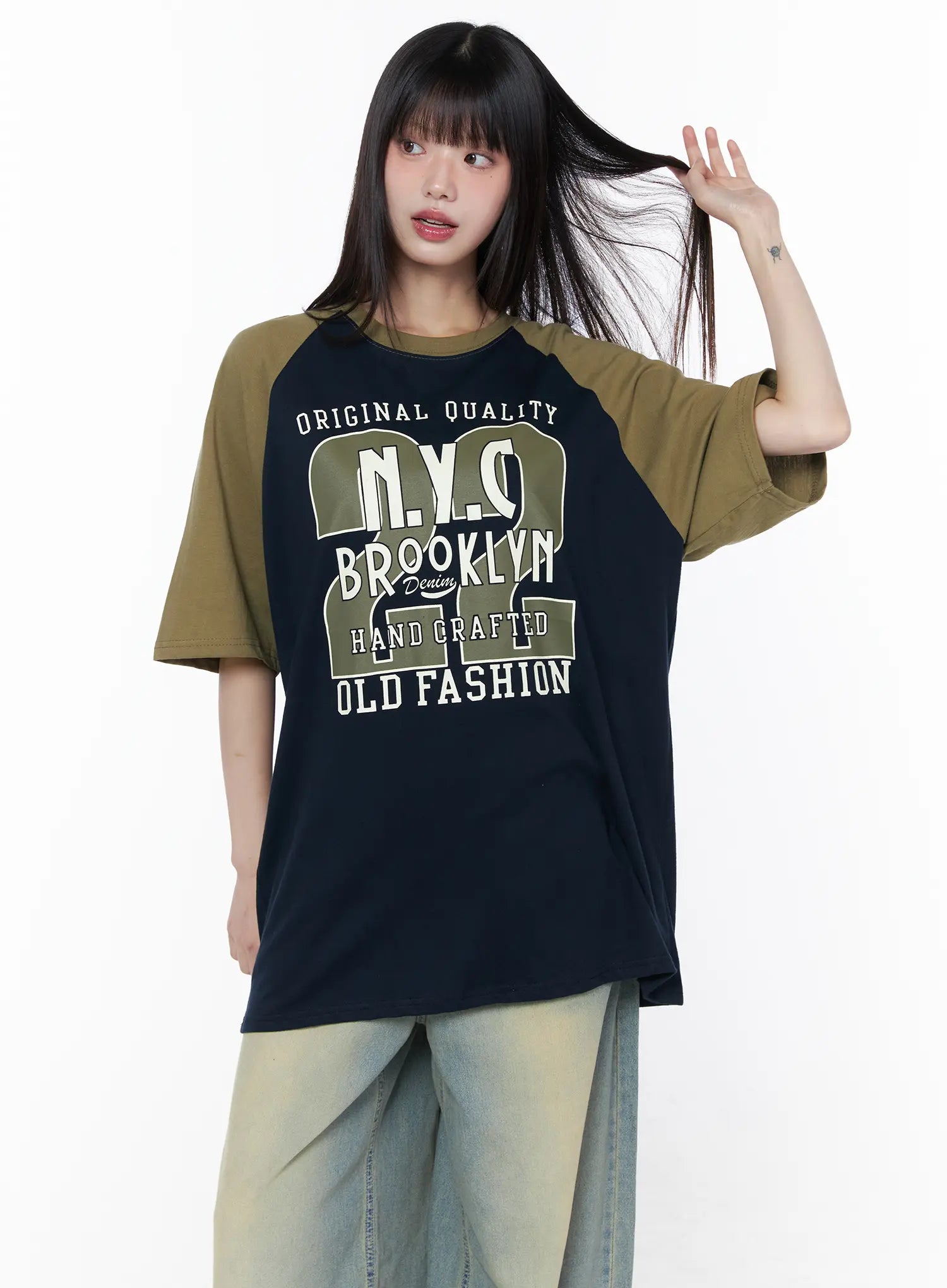 Casual Loose Fit Graphic Tee CU519 in dark blue, half-body front shot on model tossing hair, full Brooklyn NYC graphic print clearly visible, olive raglan short sleeves, crew neck, relaxed oversize fit.