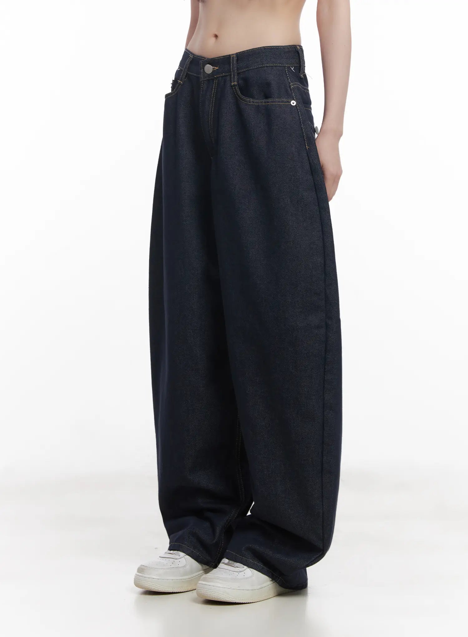 Hyein No-Fade Relaxed-Fit Jeans CU519 in dark blue, side view on model without top, highlighting voluminous wide-leg shape, contrast stitching, and front coin pocket detail with white sneakers.