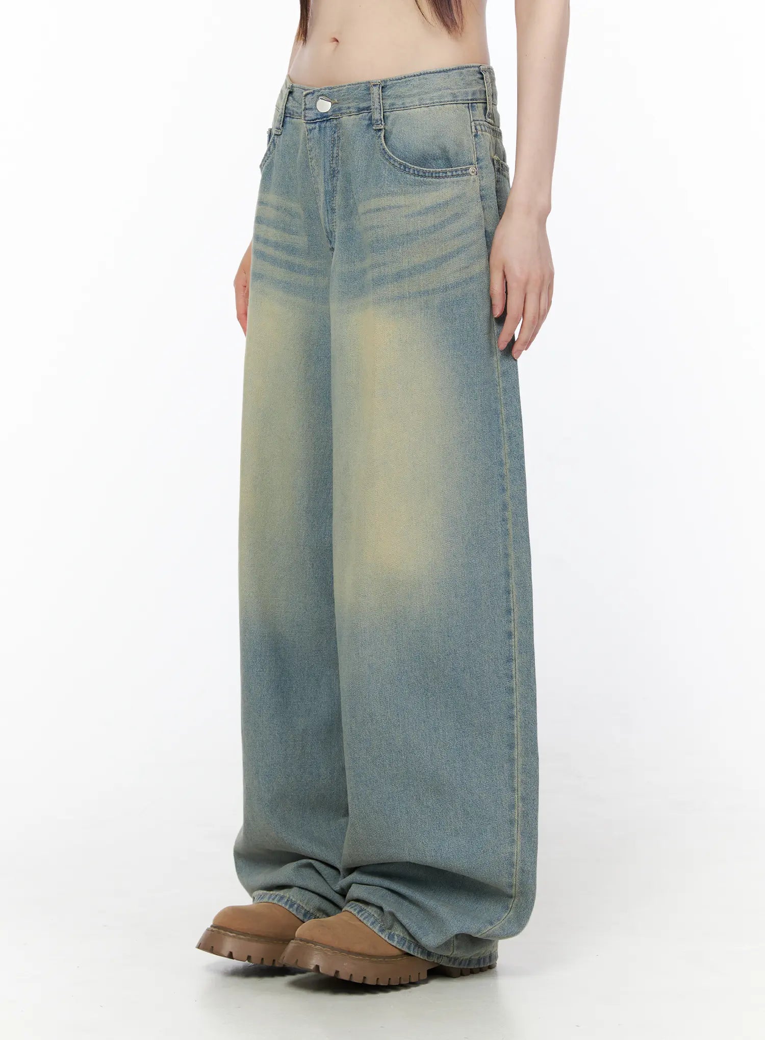 Rain Vintage Washed Wide Leg Jeans CU519 in light blue, side close-up on model, low-rise waistband, pronounced yellow vintage fade on thigh panel, wide leg draping over chunky boots.