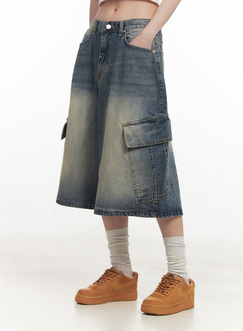 Cargo Bermuda Denim Shorts CF514 in dark blue, side angle on model from waist down, wide-fit washed denim with large flap cargo pocket, midi length, hand in front pocket, tan sneakers.