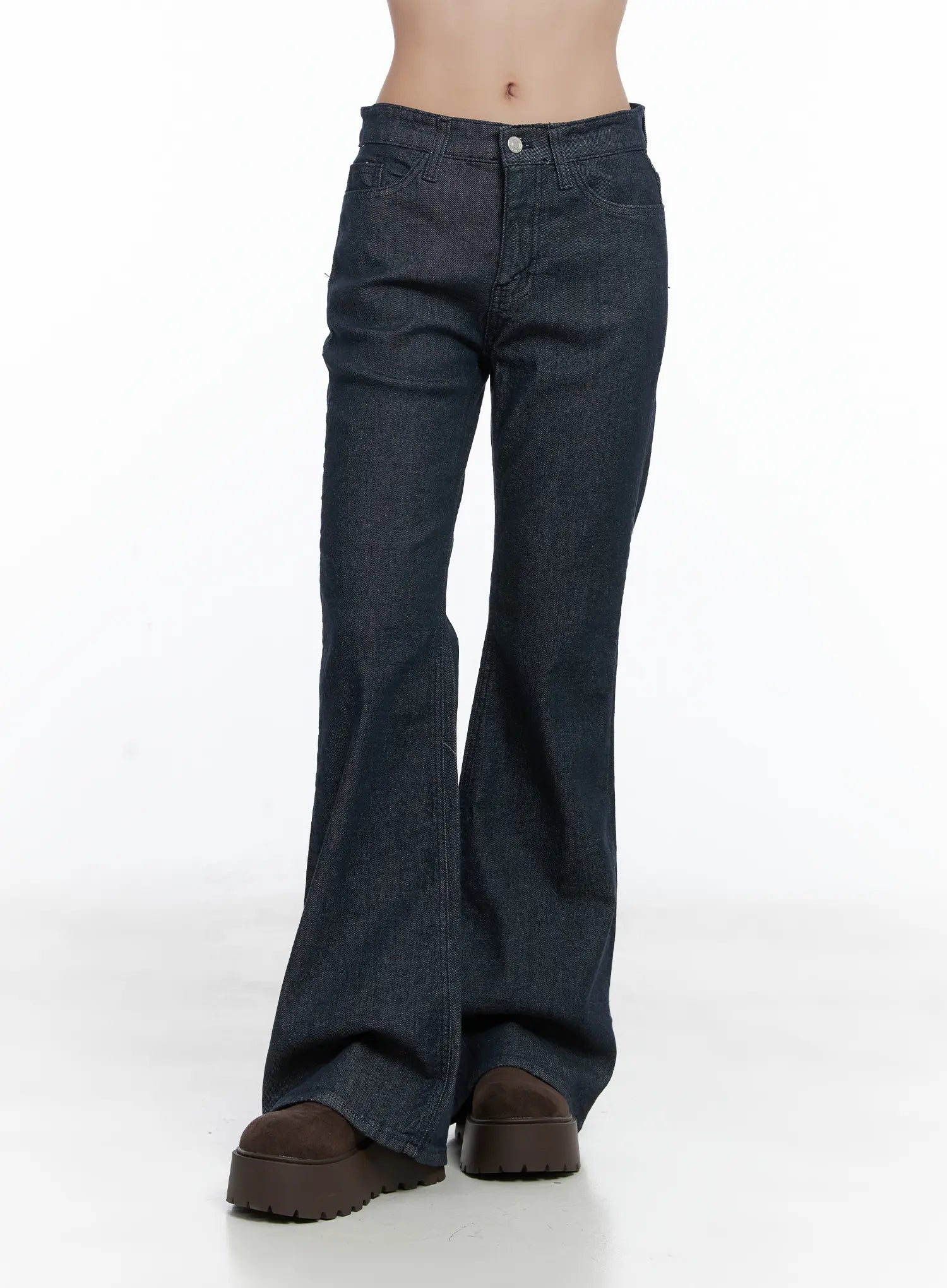 Kinley Flare Jeans CS502 in dark indigo, front lower-body crop view on model, flare leg opening at floor, front pockets and silver button, chunky boots underneath.