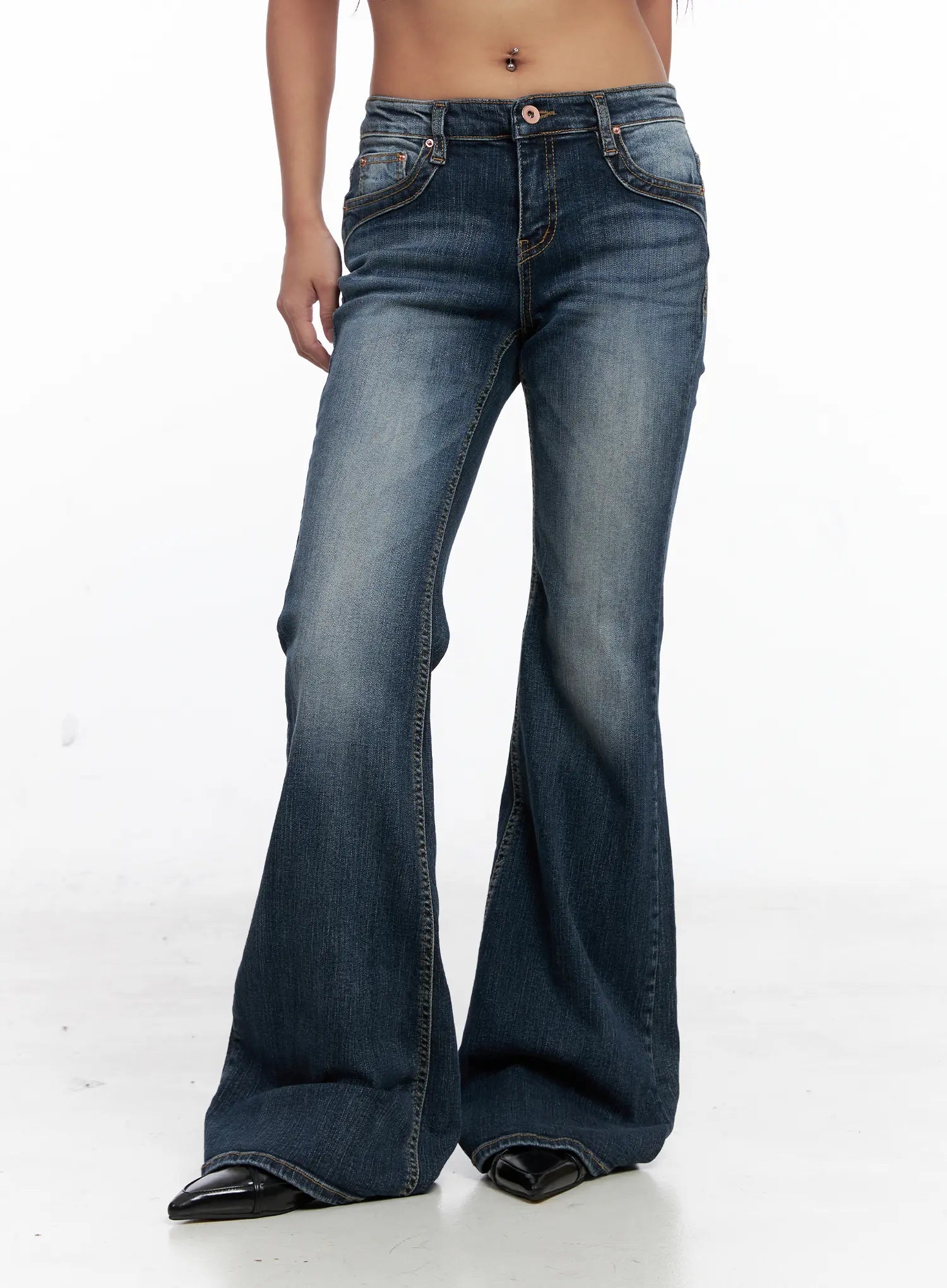 Saanvi Vintage Wash Flare Jeans CS522 in dark blue, front mid-body shot on model, low-rise waistband with button closure, front slash pockets, heavy vintage wash fading, wide flare leg, black heels.