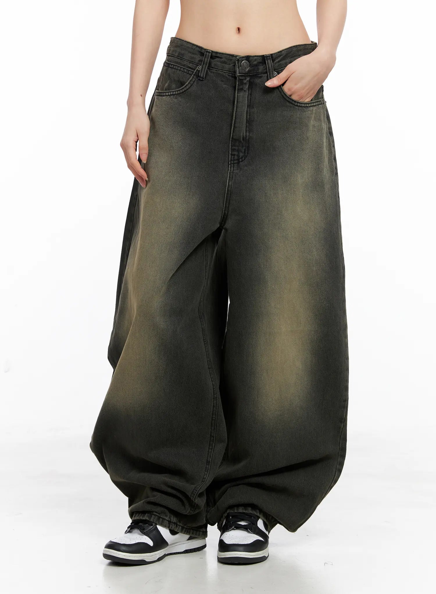 Elias Mega Wide Vintage Washed Jeans CC1109 in black, front relaxed pose on model, hand in pocket, mega wide balloon leg with heavy yellow-green wash fade and pooled hem over sneakers.