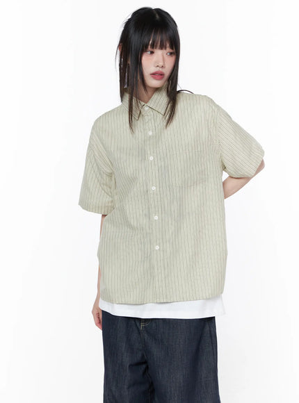 Oversized Short Sleeve Button-Up Shirt CU519 in light beige, front upper-body shot on model, striped fabric with white button-front placket and chest pocket, boxy fit layered over white tee with dark wide-leg jeans.