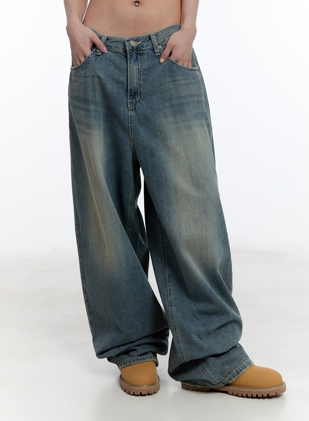Jenna Relaxed-Fit Wide-Leg Jeans CU502 in blue, front waist-to-hem crop on model, thumbs hooked in low-rise waistband, washed cotton denim with baggy leg bunching over tan boots.