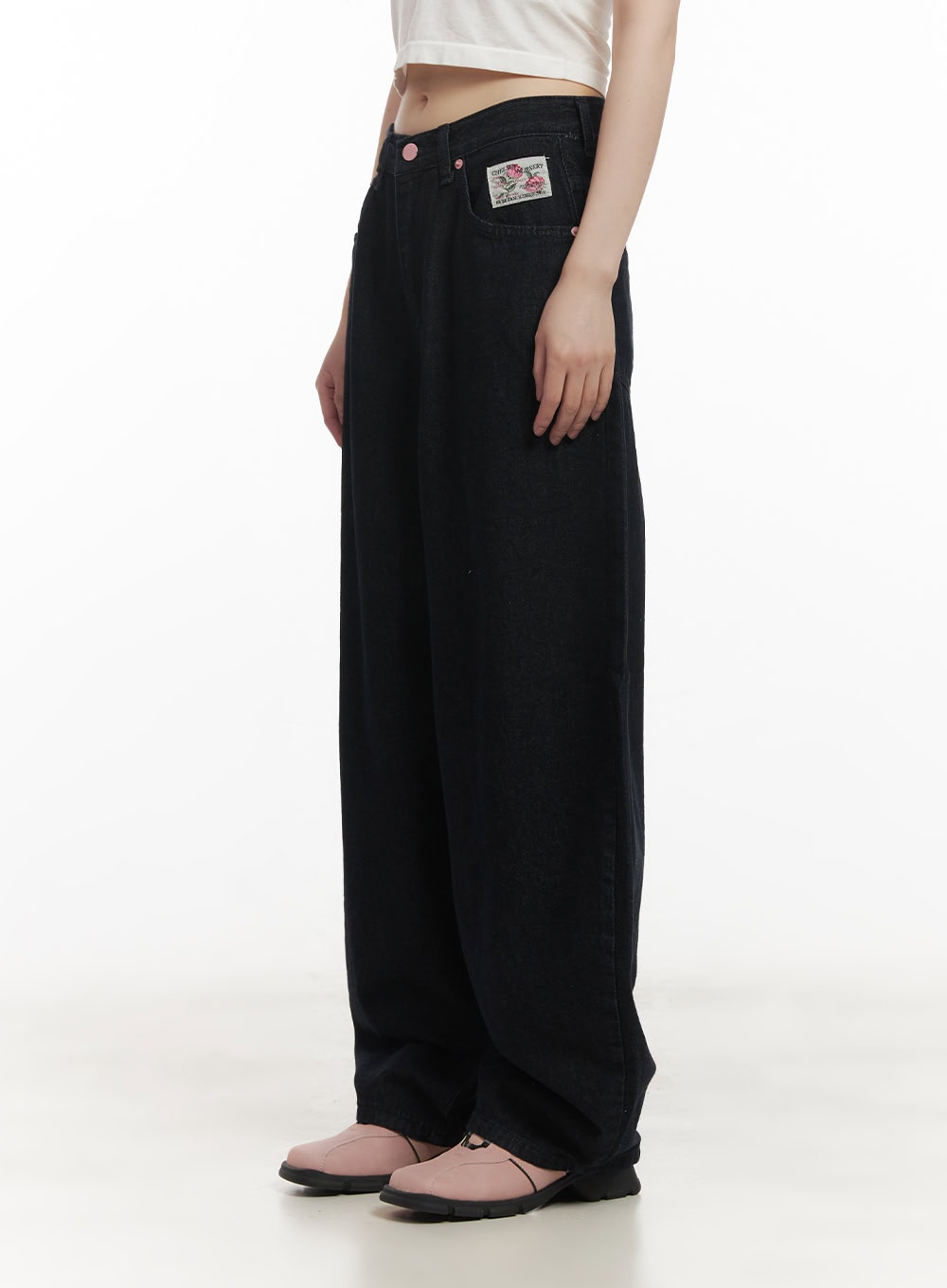Dory Embroidered Baggy Jeans CF518 in dark blue, side view on model showing floral patch label on front pocket, pink rivet button, and relaxed wide-leg cotton denim silhouette.