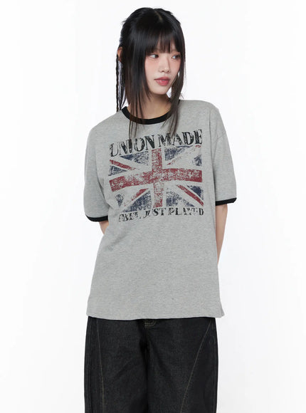 Graphic Short Sleeve Tee CU519 in gray, upper-body three-quarter view on model, vintage-style Union Jack graphic and black ringer trim, relaxed cotton tee, styled with dark wide-leg jeans.