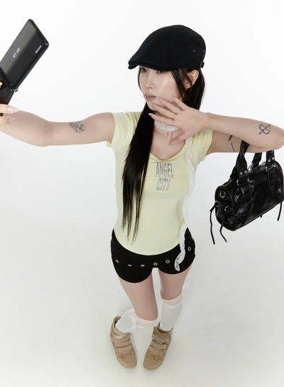 LEWKIN Angel Slim T-Shirt IL522 Light yellow overhead front shot model posing with flip phone and black bag wearing slim ribbed tee with glitter ANGEL CITY graphic
