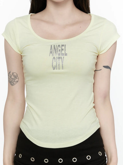 Angel Slim T-Shirt IL522 Light yellow close-up front crop model wearing slim ribbed scoop neck tee with large silver glitter ANGEL CITY graphic at chest