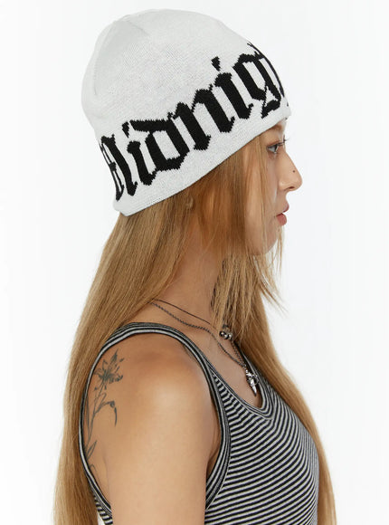 Aspen 1988 beanie IL503 White side profile view on model facing left displaying full gothic jacquard lettering on white knit