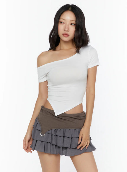 Asymmetric One-Shoulder Top CU529 White three-quarter front shot on model looking away, off-shoulder ribbed crop top with asymmetric hem styled with tiered ruffle mini skirt