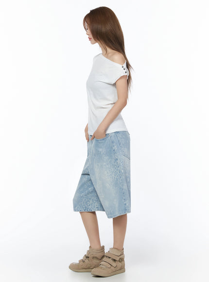 Asymmetric One-Shoulder Top IU525 White side full-body shot on model showing asymmetric off-shoulder neckline and button detail with denim shorts