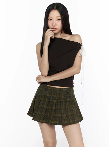 Asymmetric Shirred Off-Shoulder Top CL524 Dark brown front shot on model with hand raised to chin, ruched one-shoulder crop top with white ribbon tie, styled with green plaid mini skirt
