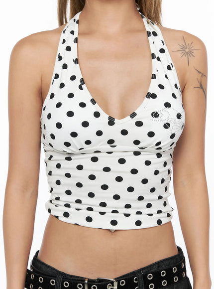 Baddie Polka Dot Halter Top CU524 White close-up front detail shot on model showing deep V-neckline, rhinestone emblem, black polka dots on white fabric, ruched hem
