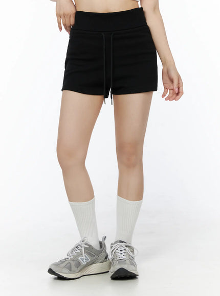 Basic Drawstring Lounge Shorts IU525 Black front close-up on model with hand at waist showing drawstring, ribbed waistband and fleece fabric texture