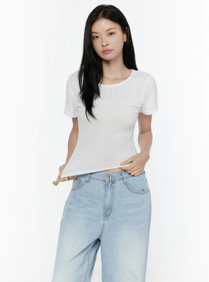 Basic Round Neck Tee IL506 White three-quarter front model shot, model holding hem to show crop length and ruched side seam detail with striped wide-leg jeans