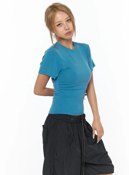 Basic Short Sleeve Top CU523 Blue S/M — 3/4 angle shot, model wearing fitted teal crop tee with black shorts, arms behind back