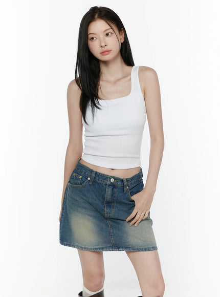 Basic Tank Top IL506 White three-quarter front shot on model looking away hand resting on thigh showing square neck ribbed crop top with faded denim mini skirt