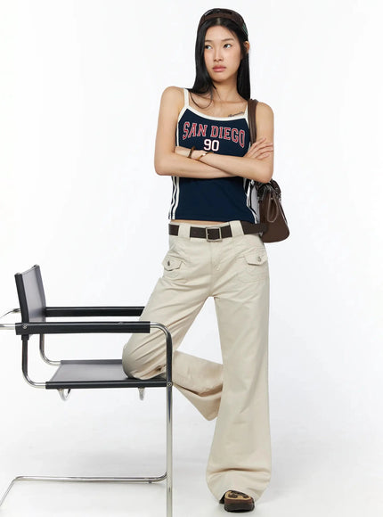 Bootcut Cargo Pants IL516 Light beige full-length styled shot, model leaning on chair arms crossed, belted with navy graphic tank and brown bag