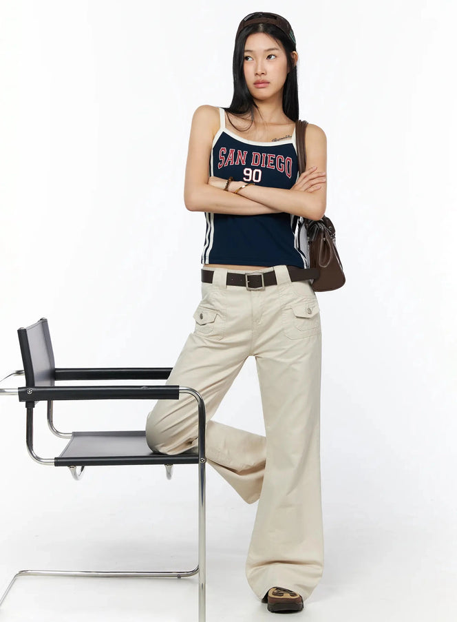 Bootcut Cargo Pants IL516 Light beige full-length styled shot, model leaning on chair arms crossed, belted with navy graphic tank and brown bag