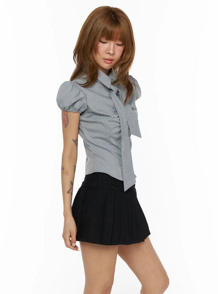 Bow Detail Puff Blouse CL503 Gray three-quarter side shot on model looking down, long bow tie detail, puff sleeves, pinstripe cotton fabric, styled with black pleated mini skirt