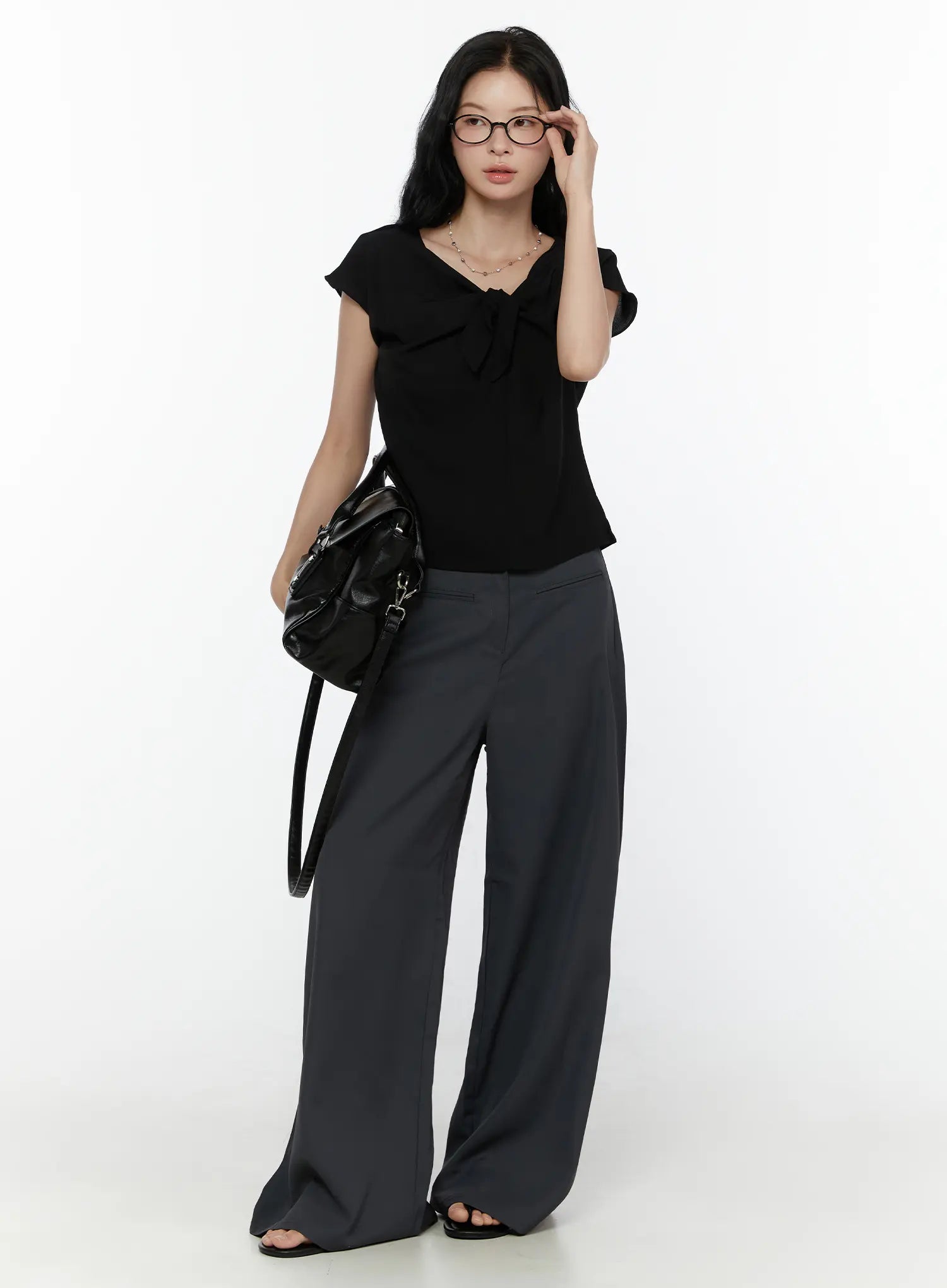 Bow Tie Cap Sleeve Blouse CL520 Black full-body front shot on model adjusting glasses styled with grey wide-leg trousers and black bag