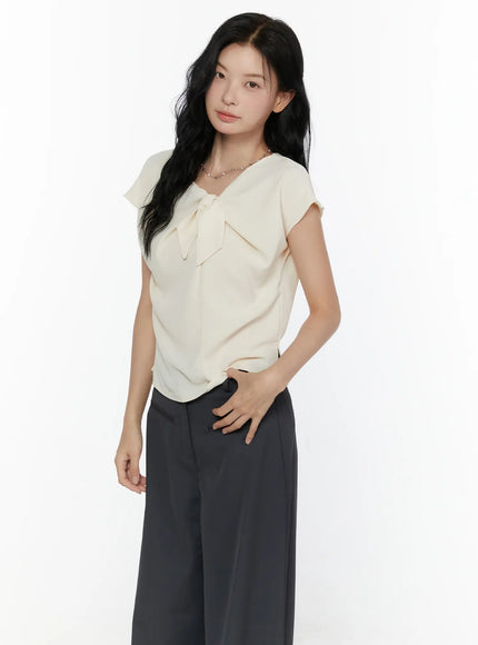 Bow Tie Cap Sleeve Blouse CL520 Cream angled front shot on model hand on hip showing bow tie neckline and draping lightweight fabric