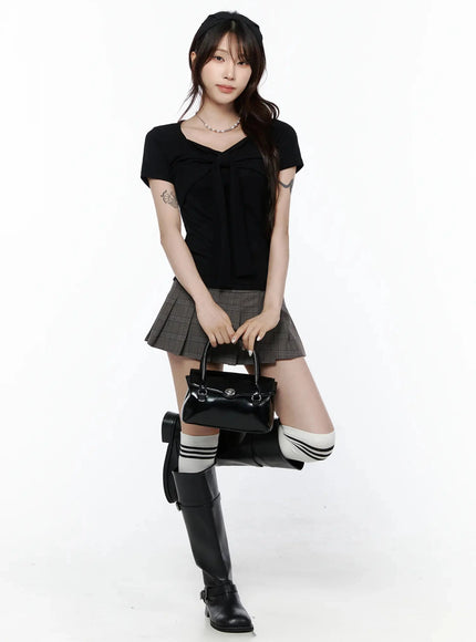 Bow Top IL506 Black front full-body styled shot on model holding black handbag with one knee raised, silver necklace, headband, and knee-high boots