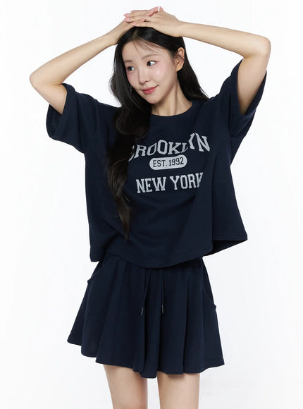Brooklyn Grahic Tee & Mini Skort Set IU525 Dark blue front view on model with hands raised above head, boxy cropped tee and flared mini skort set
