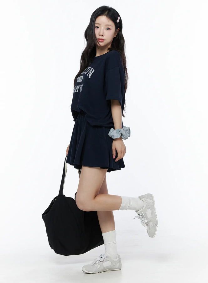 LEWKIN Brooklyn Grahic Tee & Mini Skort Set IU525 Dark blue side view on model styled with tote bag and sneakers, cropped boxy tee with collegiate graphic