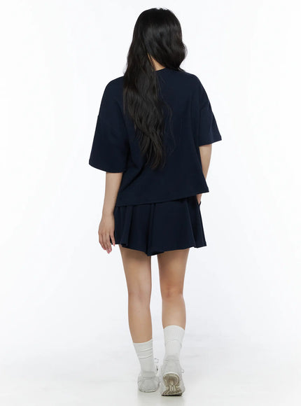 Brooklyn Grahic Tee & Mini Skort Set IU525 Dark blue back view on model showing plain navy back of cropped tee and pleated mini skort with sneakers