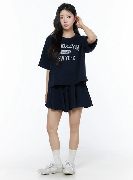 Brooklyn Grahic Tee & Mini Skort Set IU525 Dark blue full-body front view on model touching hair, complete matching navy set with sneakers and white socks