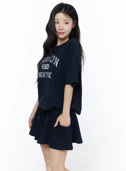 Brooklyn Grahic Tee & Mini Skort Set IU525 Dark blue angled side view on model showing layered cropped tee over flared skort with white socks and sneakers