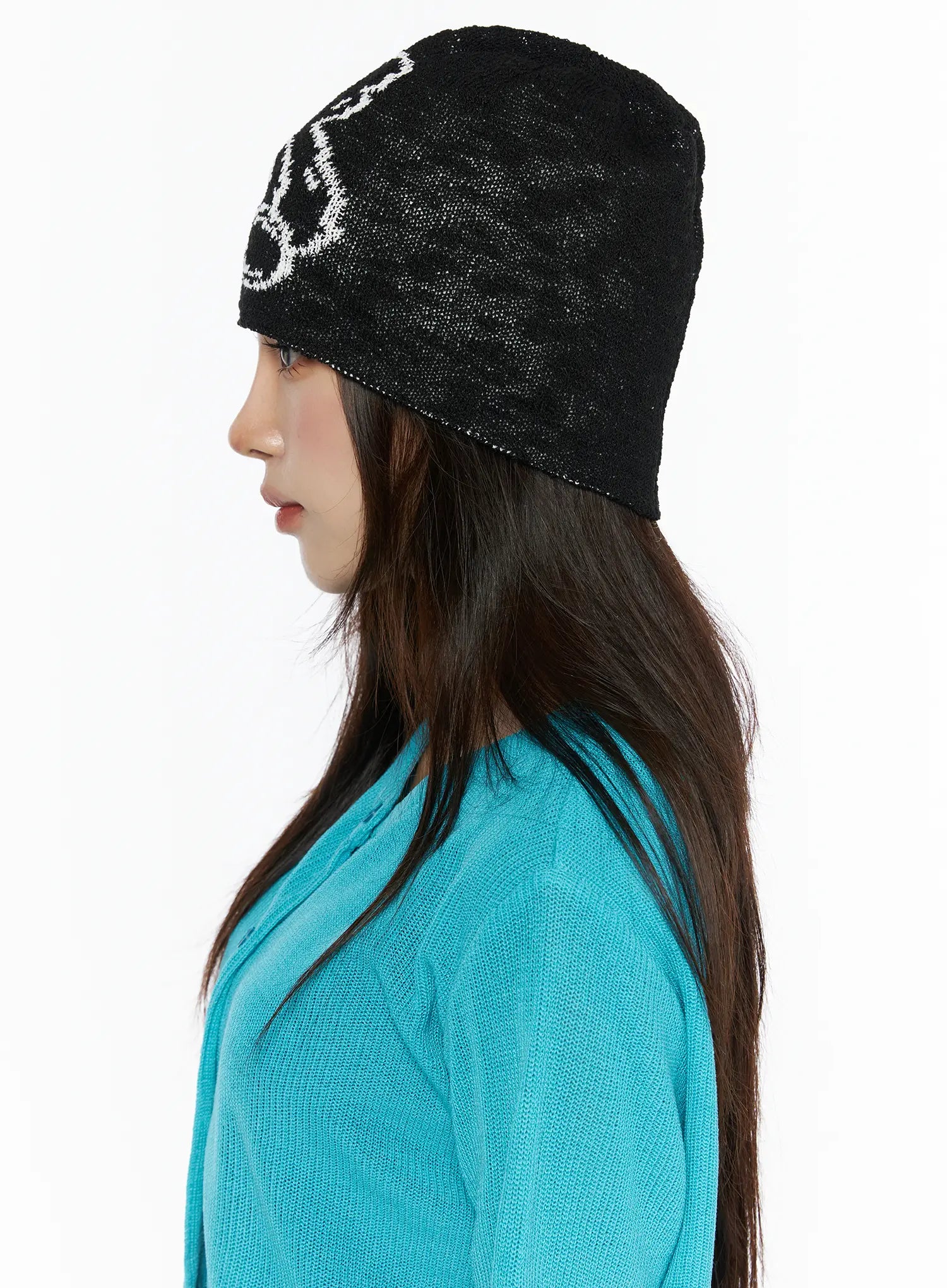 Brooks Bear Beanie IL503 Black side profile shot on model wearing teal knit top, semi-sheer black knit beanie with white bear graphic at temple