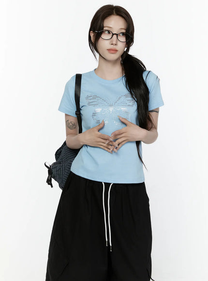 Butterfly Graphic Crop Tee IL521 Light blue front view on model with hands clasped at waist styled with black wide-leg pants and backpack