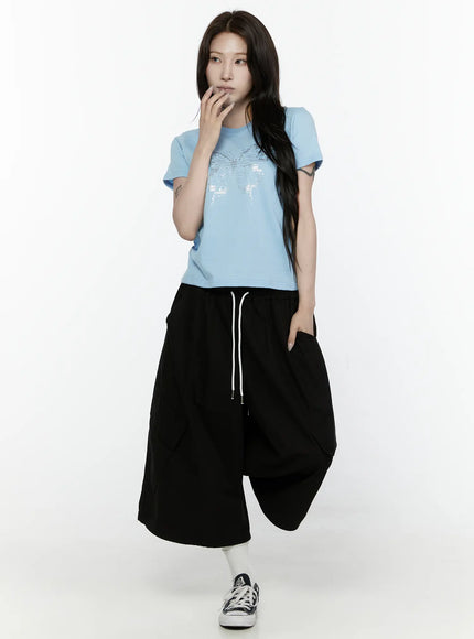 Butterfly Graphic Crop Tee IL521 Light blue front view on model with hand near chin styled with black drawstring wide-leg pants and canvas sneakers