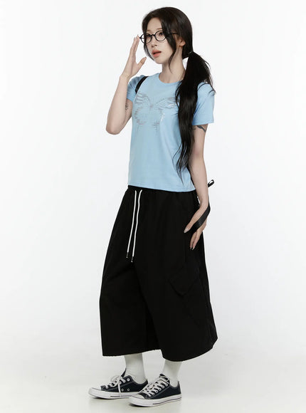 Butterfly Graphic Crop Tee IL521 Light blue three-quarter side view on model with hand raised styled with black wide-leg cargo pants and sneakers