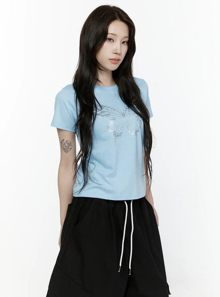 Butterfly Graphic Crop Tee IL521 Light blue three-quarter front view on model with long hair down showing silver butterfly rhinestone graphic and crew neckline