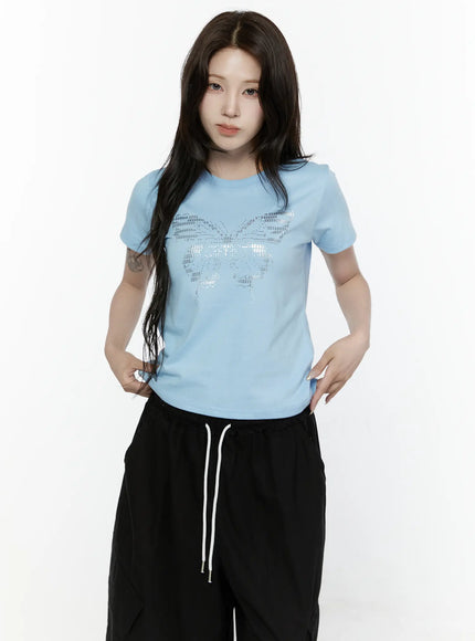 Butterfly Graphic Crop Tee IL521 Light blue front view on model with hands on hips showing fitted cropped silhouette and silver butterfly rhinestone graphic