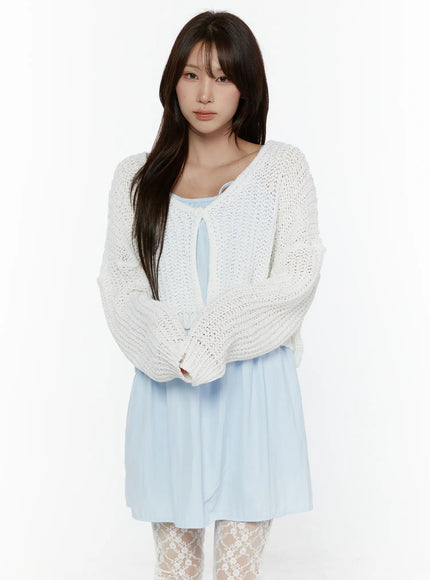 Button Knit Cardigan CL508 White front half-body shot on model with arms crossed, showing open-knit texture, cropped hem, and long balloon sleeves over light blue dress