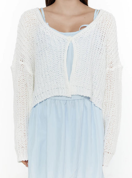 Button Knit Cardigan CL508 White close-up front detail on model showing chunky open-knit weave, single button tie closure, cropped silhouette, and ribbed hem over blue dress
